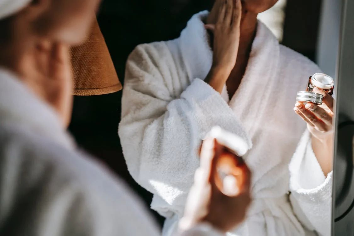 Mujer en bata de baño aplicándose una crema facial frente al espejo